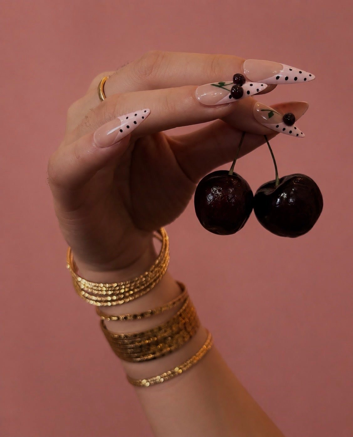 A hand with cherry painted Roselia nails holding two real cherries
